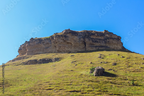 round stone rock and base covered with grass against the blue sky