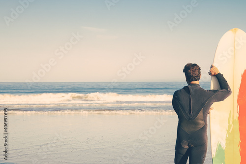 Photography Back view of brunette surfer standing with surfboard on beach