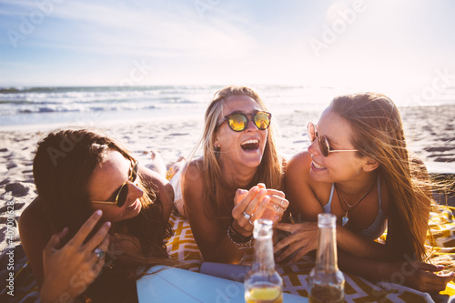 Happy girlriends chatting and laughing on the beach drinking beer photo