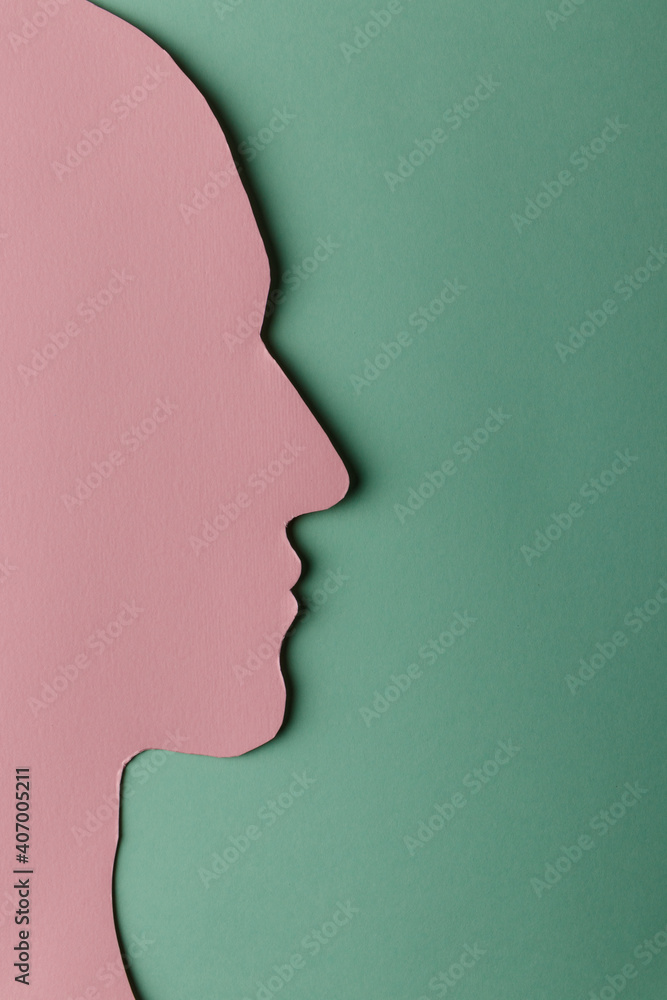 Head silhouette made of paper. Pink paper shaped as a human head with copy space on green paper background.