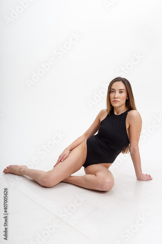 sexy asian woman with long hair posing in black lingerie on white studio background with bare feet. attractive female sitting on floor with her knees bent. model tests of skinny lady in bodysuit