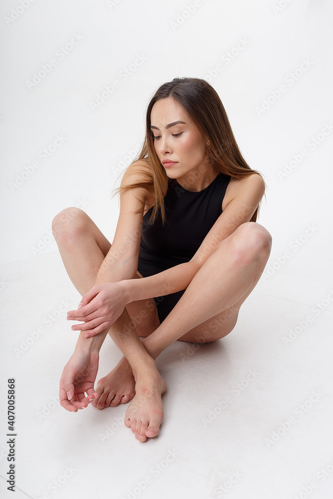sexy asian woman with long hair posing in black lingerie on white studio background with bare feet. attractive female sitting on floor with her knees bent. model tests of skinny lady in bodysuit sexy asian woman with long hair posing in black lingerie on white studio background with bare feet. attractive female sitting on floor with her knees bent. model tests of skinny lady in bodysuit