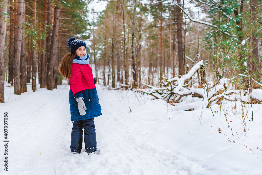 Little girl in a red jacket standing in the middle of a path in a winter pine forest