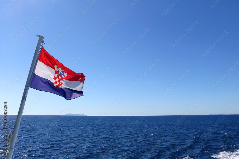 Fototapeta premium Flag of Croatia, blowing in the wind. Adriatic sea and bright sky in the background. Selective focus.