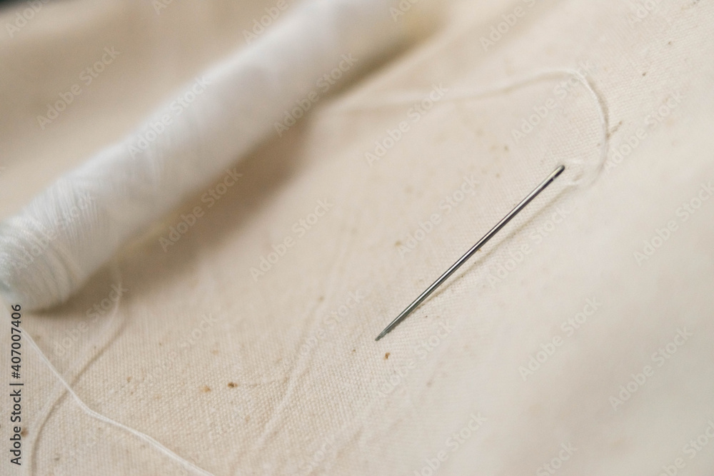 Needle with thread. Spool of thread. Sewing. Sewing machine. Seamstress. Sewing. White threads. Handmade. The cloth.