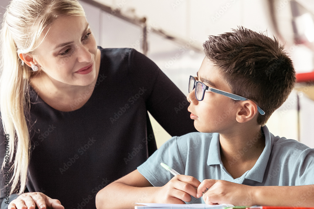 Cheerful school teacher giving help and support to schoolboy in class. Front view. Education or back to school concept Cheerful school teacher giving help and support to schoolboy in class. Front view. Education or back to school concept