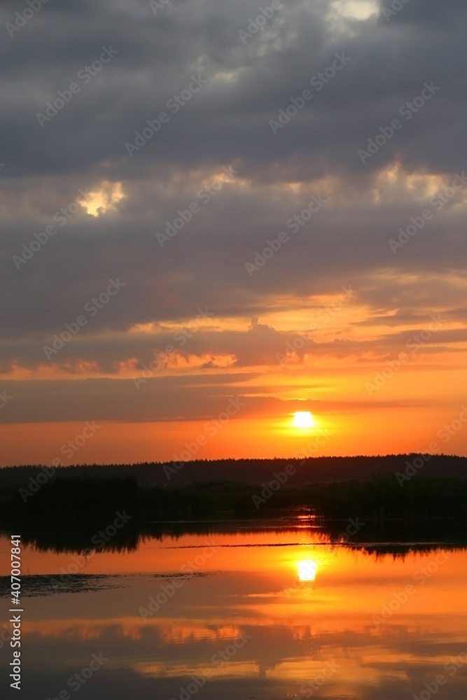 Red sunset over a calm summer lake. The top of the photo is taken up by a cloudy sky.
