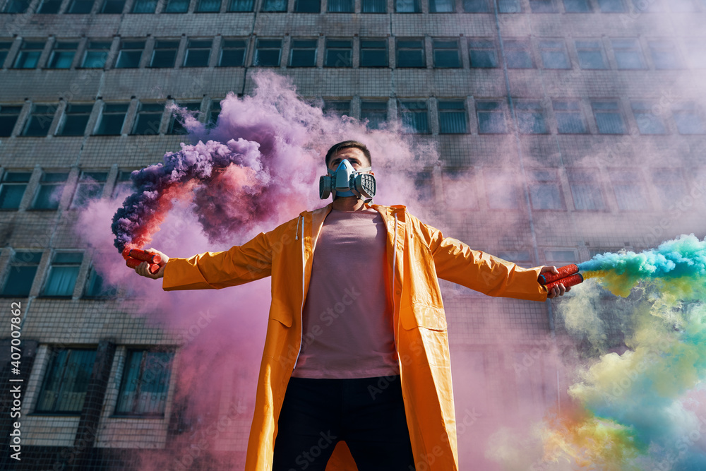 Obraz premium Young man in respirator mask hold smoke bombs in raised hands