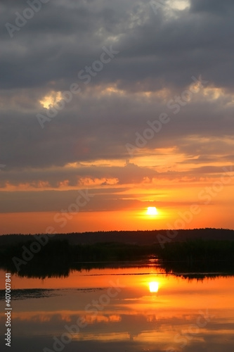 Red sunset over a calm summer lake. The top of the photo is taken up by a cloudy sky.