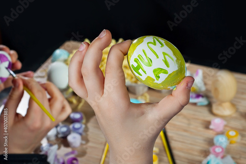 Mother and son paint Easter eggs. Multi Colored Easter eggs on a wooden table background. Traditional family entertainment before the holiday. An egg with the inscription "Human" in a boy's hand.