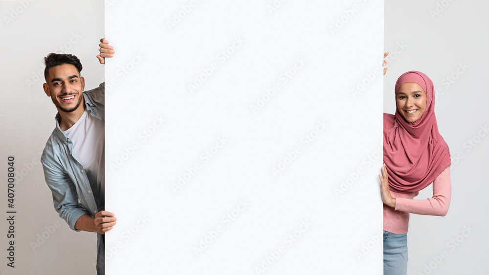 Smiling young muslim couple holding white advertisement board, demonstrating copy space Smiling young muslim couple holding white advertisement board, demonstrating copy space