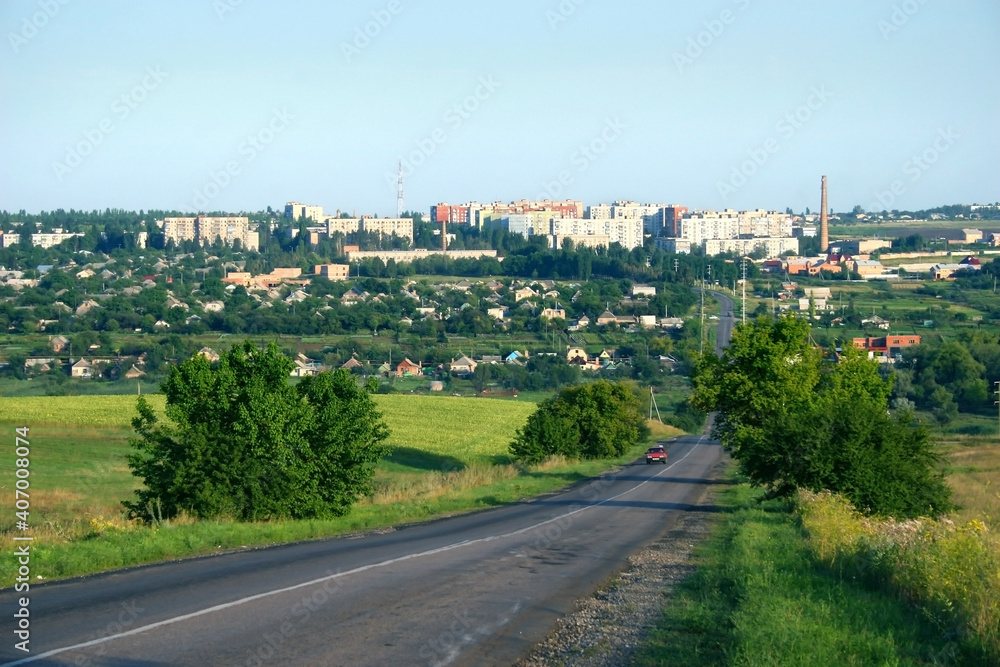 View of the Ukrainian city of Bakhmut. In the distance there is an asphalt road on which the car is driving. The skyline is formed by urban development.