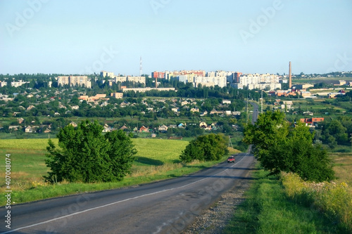 View of the Ukrainian city of Bakhmut. In the distance there is an asphalt road on which the car is driving. The skyline is formed by urban development.
