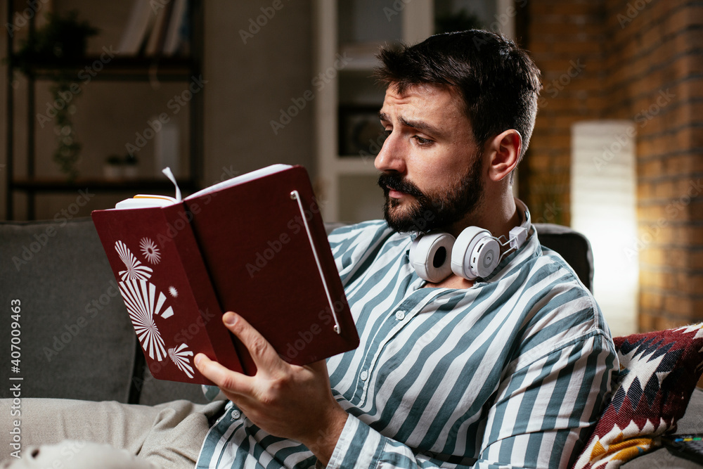 Man at home studying. Young man reading a book on the couch.