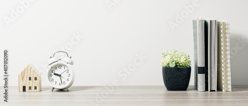 Workspace with book, clock and tree pot on wood table with living room white wall. Panoramic banner of workplace with copy space