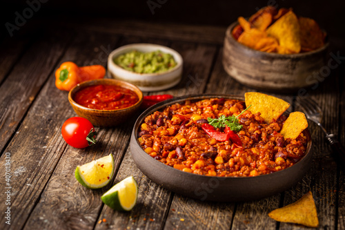 Mexican hot chili con carne in a bowl with tortilla chips on wooden background