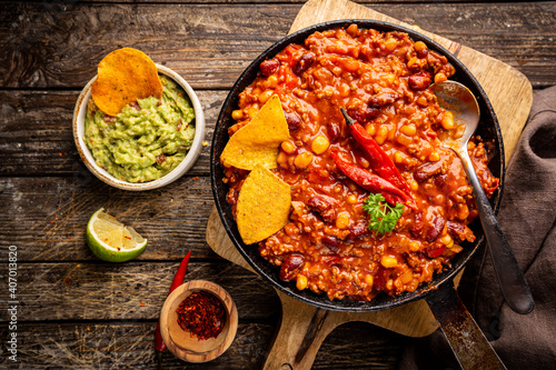Bilde på lerret Mexican hot chili con carne in a pan with tortilla chips on dark background, top