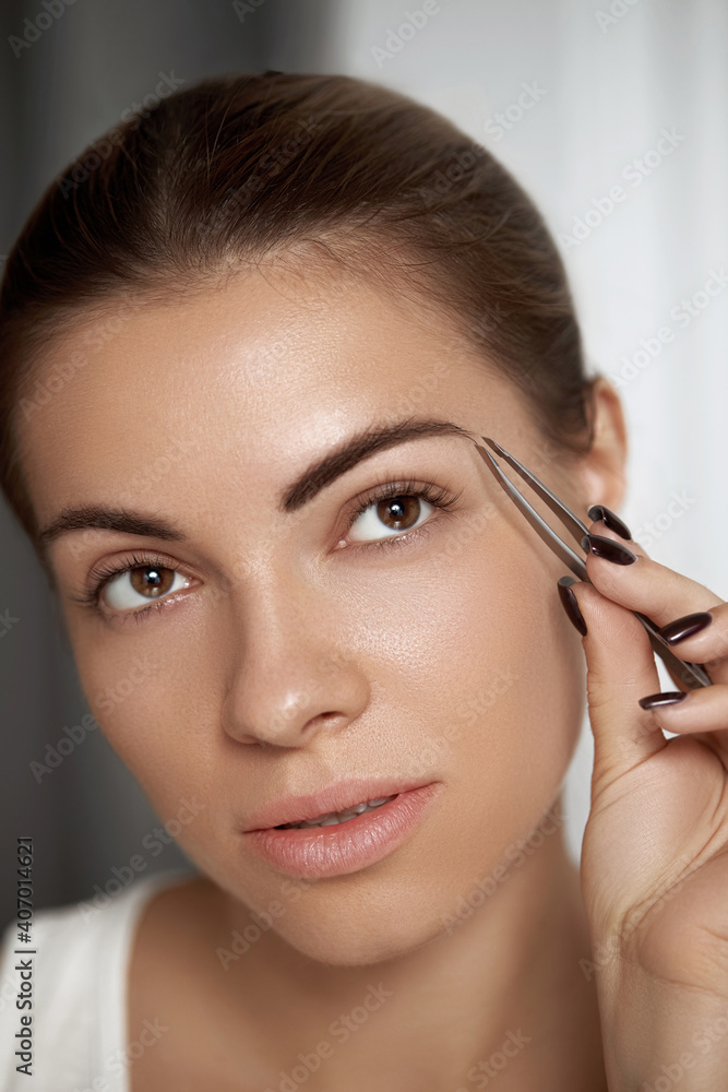 Eyebrow correction.  Plucking eyebrows. Beautiful young woman with tweezers. Model with beauty Face.