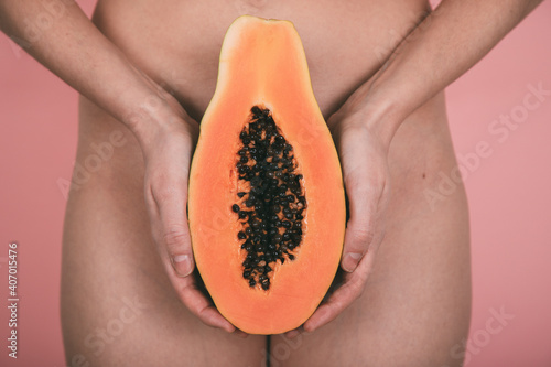 woman's hands holding a papaya in front of the hips with pink background. concept femininity. concept empowerment photo