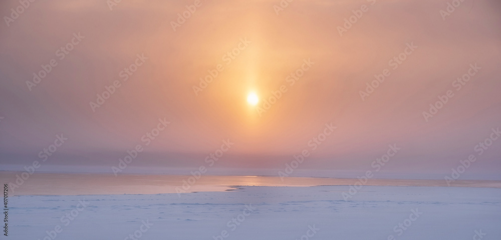 Winter background, Sun in a haze at sunset over a frozen lake in snow and ice