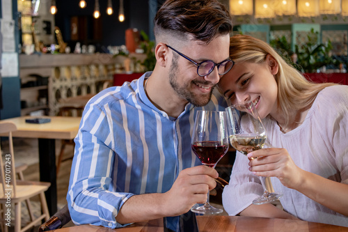 Happy young romantic couple in love, toasting with wine glasses at dinner in a beautiful restaurant.