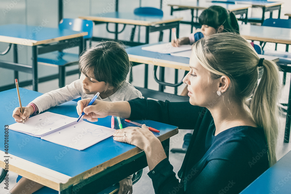 Serious school teacher helping pupils to cope with their task in class. Education or back to school concept