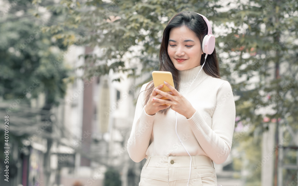 Asian woman chatting on mobile phone, wearing headphone and listening to music Asian woman chatting on mobile phone, wearing headphone and listening to music