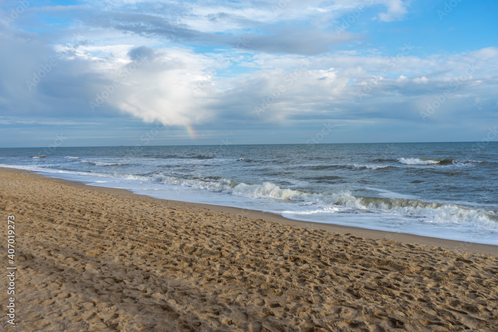 Coast with a wave rolling over it and a rainbow in the sky