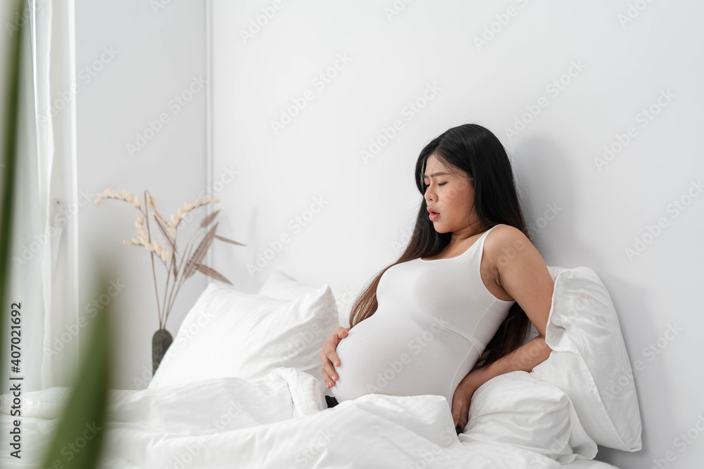 pregnant asian woman suffering from back pain. beautiful pregnant woman touching her tummy and keeping one hand on her back pregnant asian woman suffering from back pain. beautiful pregnant woman touching her tummy and keeping one hand on her back