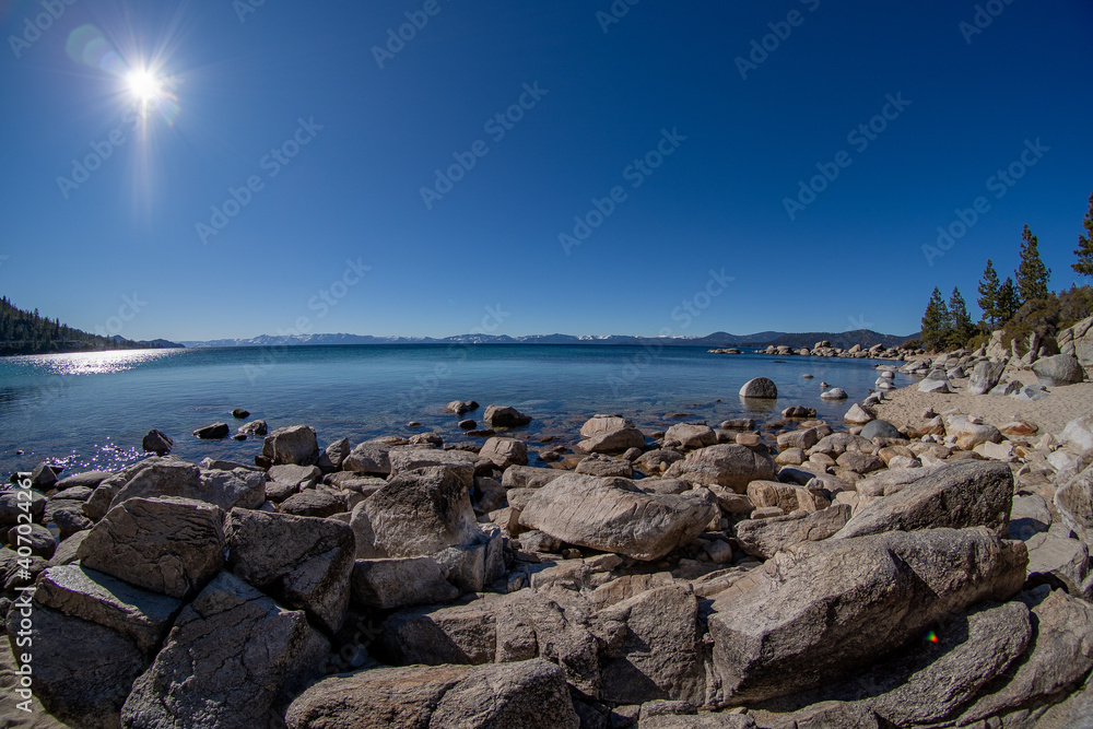 Fisheye pictures of a lake shore with rock, driftwood and bright sunshine