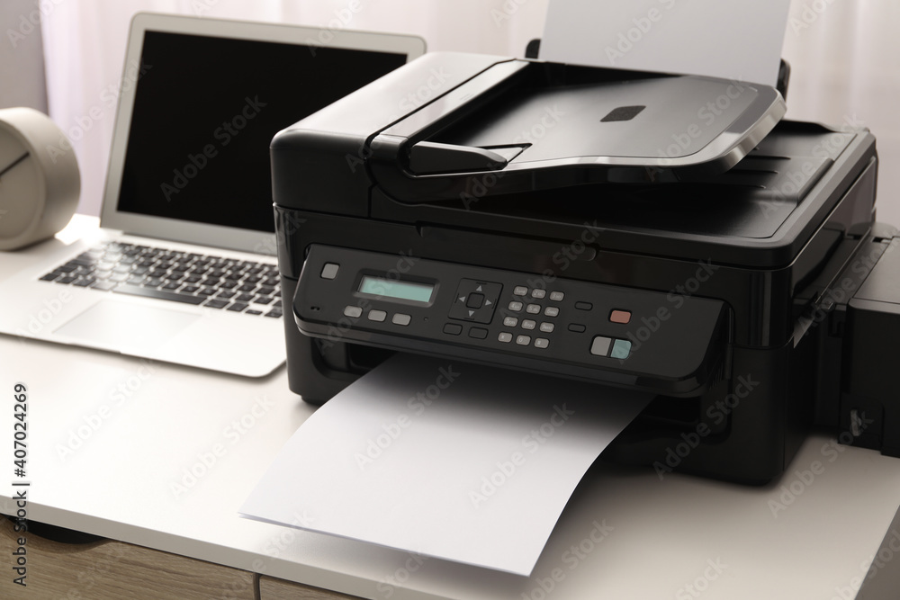 Modern printer and laptop on white table indoors Modern printer and laptop on white table indoors
