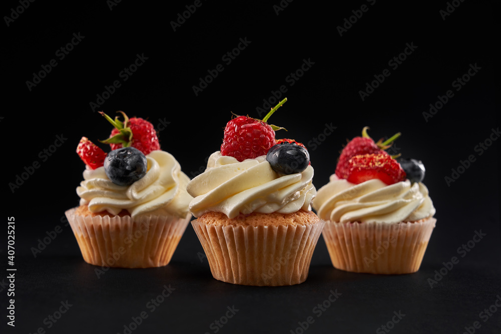 Delicious cupcakes with berries, isolated on black.