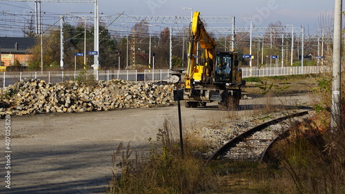 żółta koparka na placu budowy e trakcie przebudowy stacji kolejowej przy torach kolejowych w Żorach w Polsce.