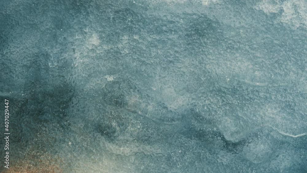 Background with grainy ice over running stream. Close-up with light from the lower left corner. Beautiful varying shades in the ice while the water flows underneath Background with grainy ice over running stream. Close-up with light from the lower left corner. Beautiful varying shades in the ice while the water flows underneath