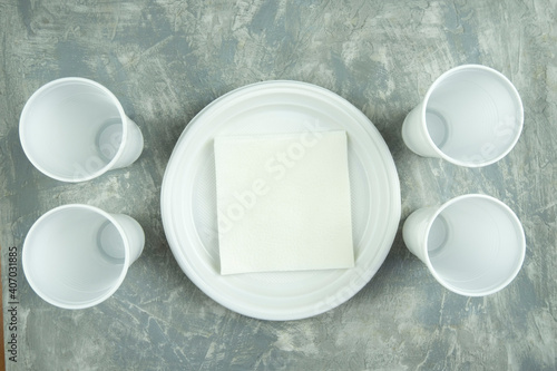 plastic dishes on a concrete background. plastic plates, forks, knives, glasses.