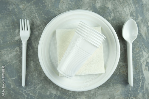 plastic dishes on a concrete background. plastic plates, forks, knives, glasses.