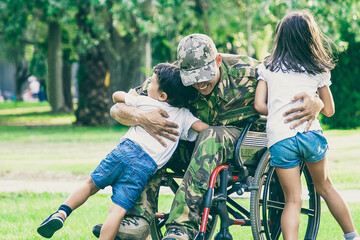 Happy disabled military man in wheelchair returning home and hugging kids. Veteran of war or family reunion concept