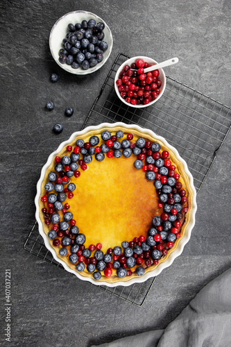 Delicious cheesecake tart with fresh blueberries and cranberries, on a dark stone background. Top view.