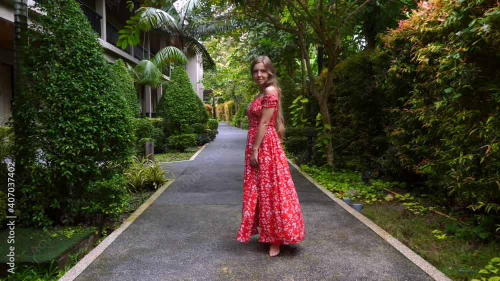 Slow Motion of Happy Smiling Travel Woman in Dress Walking and Looking at Camera in Tropical Resort. Tourist Relax and Enjoy Green Palm Trees, Bushes and Exotic Greenery on Summer Holiday in Thailand Slow Motion of Happy Smiling Travel Woman in Dress Walking and Looking at Camera in Tropical Resort. Tourist Relax and Enjoy Green Palm Trees, Bushes and Exotic Greenery on Summer Holiday in Thailand