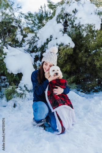 beautiful woman in snowy mountain Holding cute poodle dog in arms wrapped in plaid blanket. winter season. nature and pets