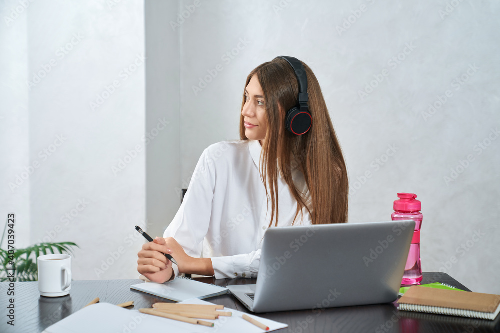 Pretty student in headphone sitting at table with laptop Pretty student in headphone sitting at table with laptop