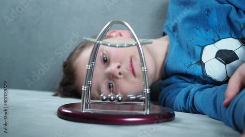 a boy plays with Newton's pendulum balls while lying on the couch. physical experiments.