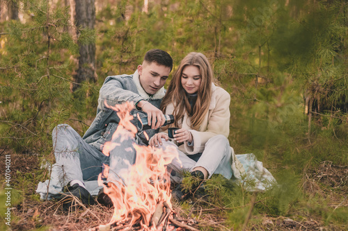  couple on a picnic in a pine forest near the fire, the guy pours the girl tea