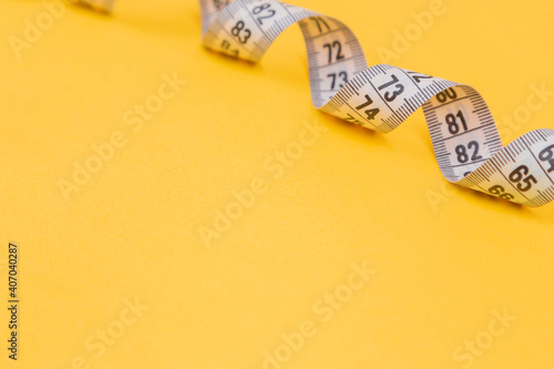 White measuring tape on a yellow background. Diet. Slimming. Obesity. Place for an inscription. Weight loss marathon. Advertising. Top view. The close plan.