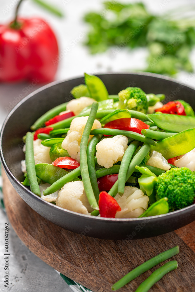 Cooked vegetables in a plate close-up. Steamed bean pods, pea pods, cauliflower, broccoli, and peppers. Healthy diet food, vegan food.