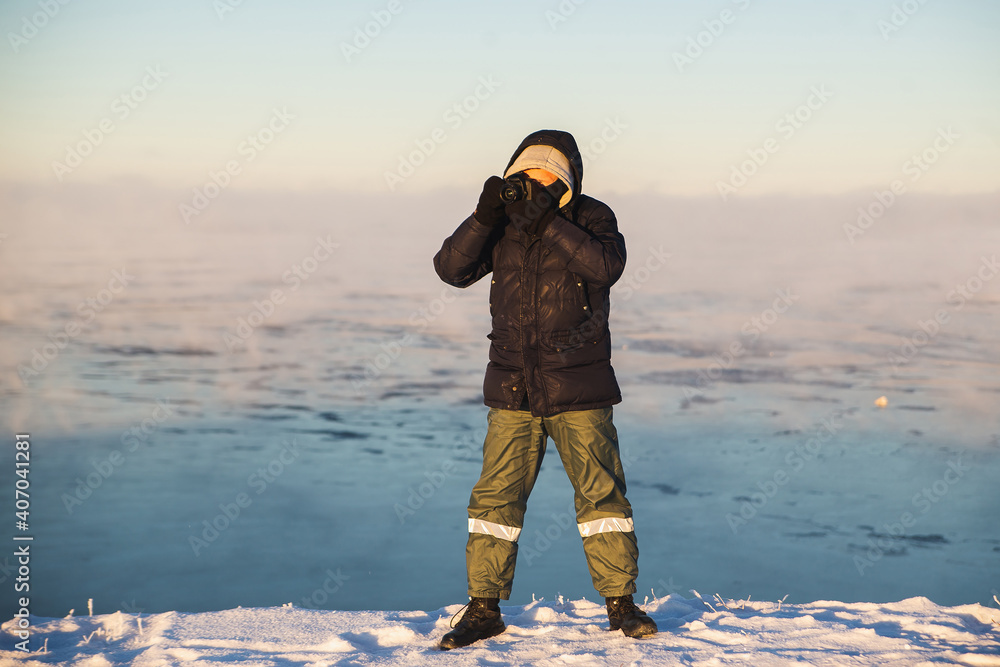 A professional photographer in warm winter clothes takes pictures of the amazingly beautiful winter nature in the bitter frost on the shore of the freezing sea