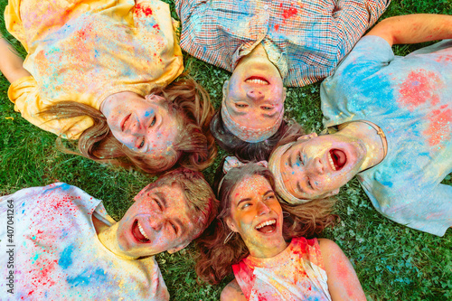 happy friends laying on green grass ground dirty in holi paints