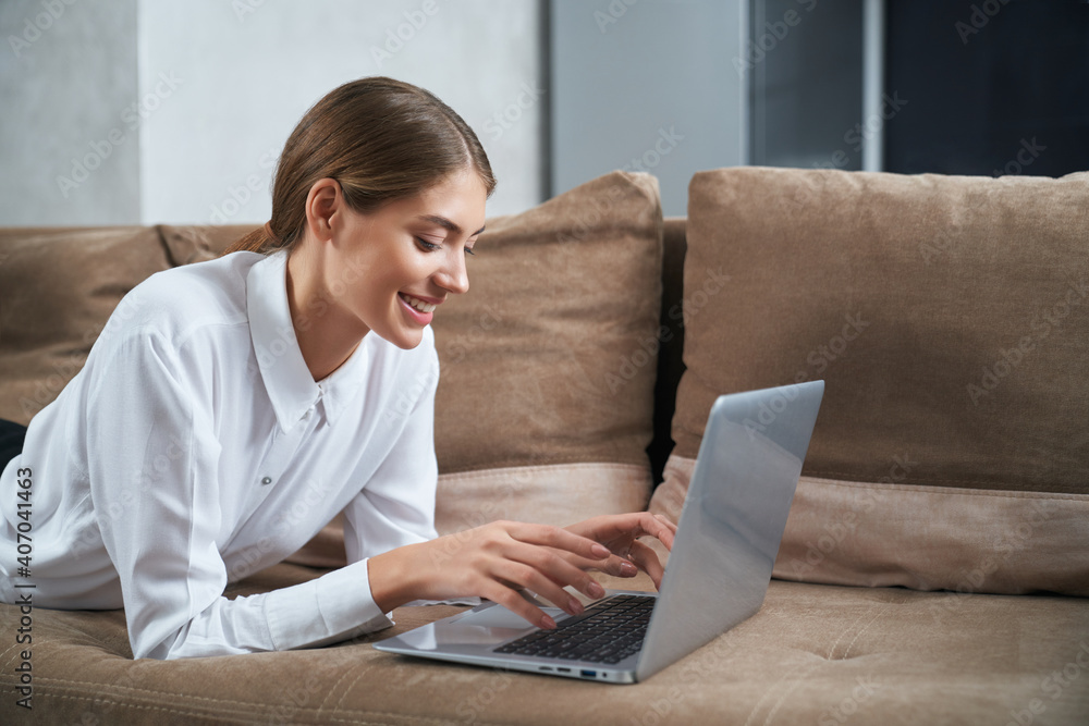 Woman typing on laptop while relaxing on couch Woman typing on laptop while relaxing on couch