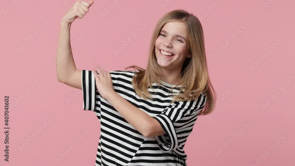Excited strong little blonde kid girl 12-13 years old wearing white black striped casual t-shirt isolated on pastel pink background studio. Childhood lifestyle concept. Showing biceps muscles on hands Excited strong little blonde kid girl 12-13 years old wearing white black striped casual t-shirt isolated on pastel pink background studio. Childhood lifestyle concept. Showing biceps muscles on hands