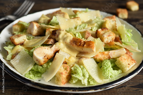 Caesar salad with lettuce, chicken and sauce on a wooden background.